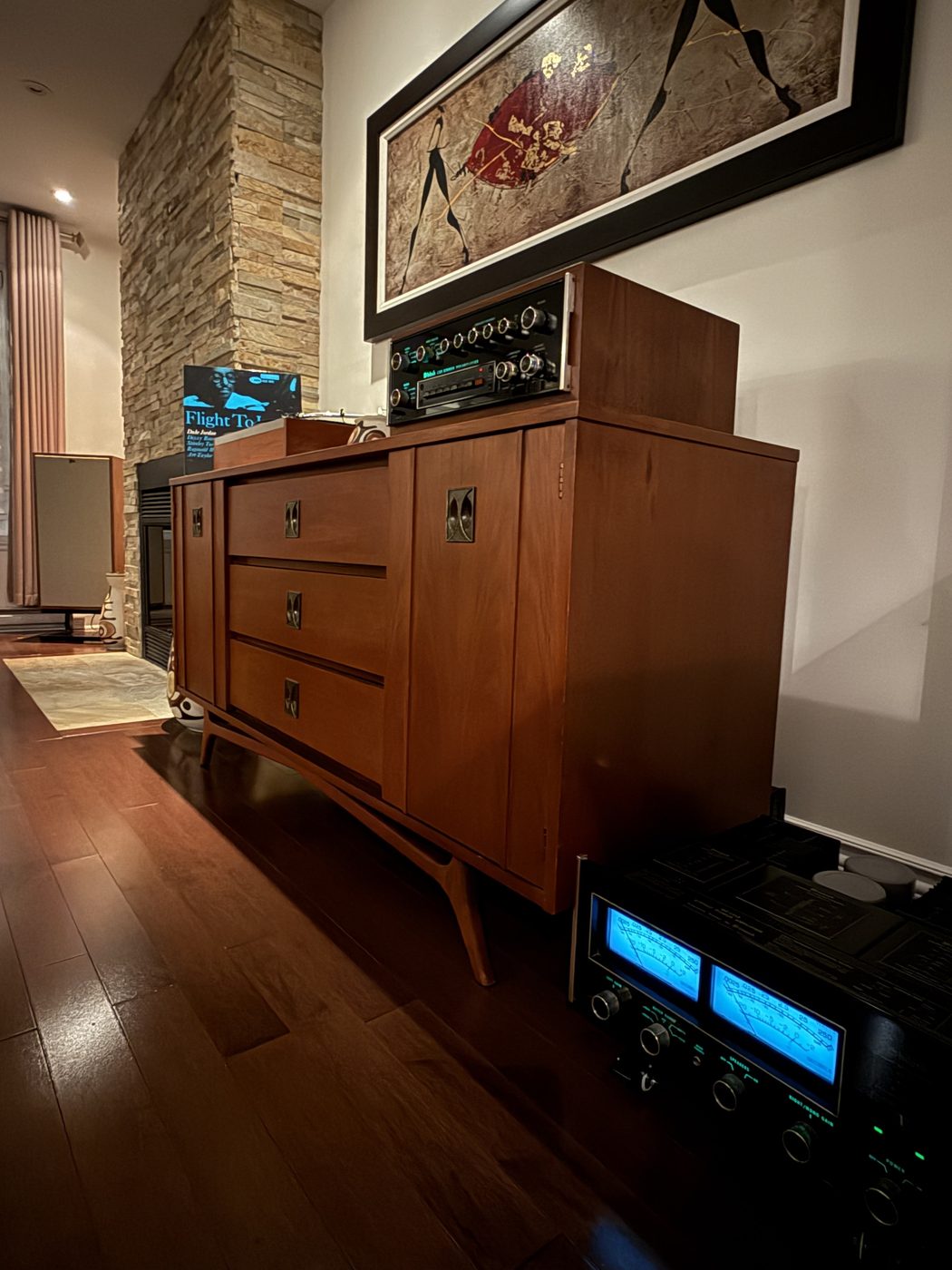 McIntosh C33 preamplifier on a mid-century walnut credenza, with the MC2255 power amplifier and its illuminated blue meters in the foreground, beside a stone fireplace
